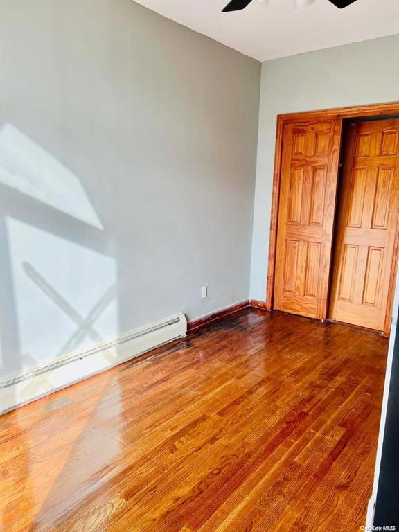 unfurnished bedroom featuring a baseboard heating unit, dark wood-style floors, and a ceiling fan