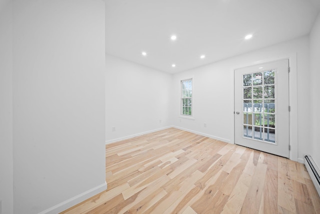 empty room featuring baseboard heating, light wood-style floors, plenty of natural light, recessed lighting, and baseboards
