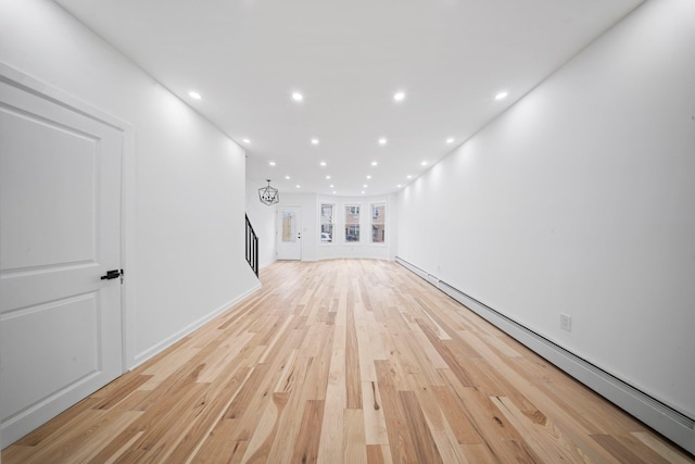 unfurnished living room featuring baseboard heating, light wood-style flooring, recessed lighting, stairs, and baseboards