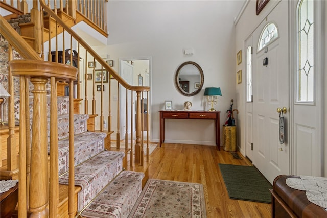 foyer entrance with stairs, light wood-style flooring, a high ceiling, and baseboards
