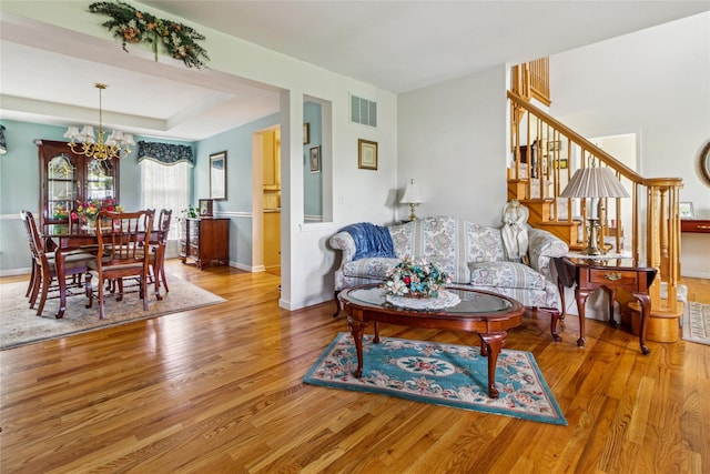 living room featuring a chandelier, wood finished floors, baseboards, and stairway