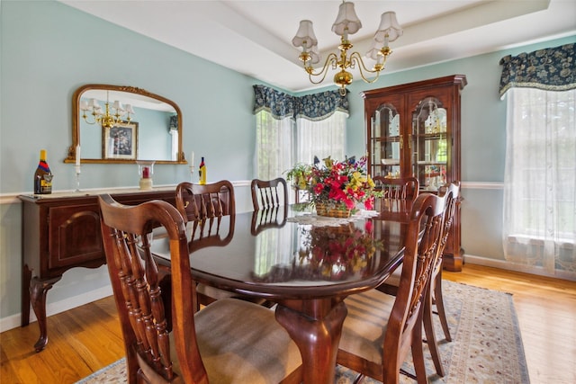dining area with a chandelier, wood finished floors, a raised ceiling, and baseboards