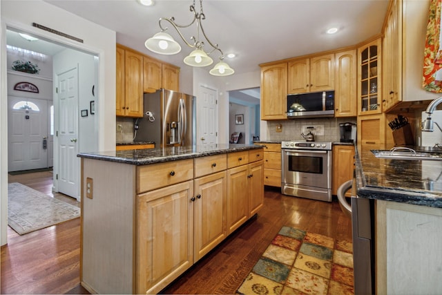 kitchen with appliances with stainless steel finishes, a sink, a center island, dark wood-style floors, and tasteful backsplash