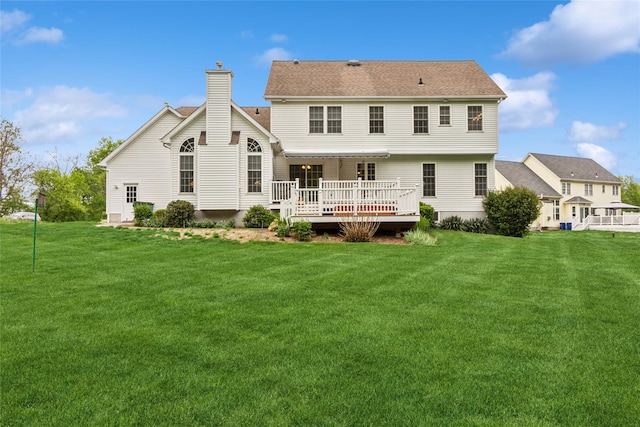 back of property with a wooden deck, a chimney, and a lawn