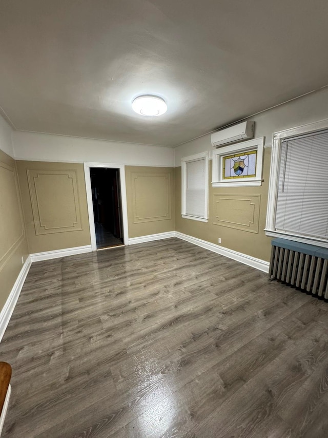 19-11 147th St, Flushing, NY 11357 - unfurnished room with a wall unit AC, dark wood-style flooring, radiator heating unit, a decorative wall, and baseboards