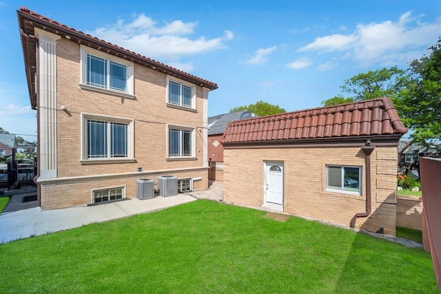 back of property with a tile roof, central AC unit, brick siding, and a lawn