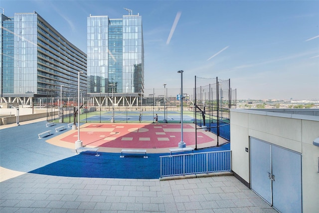 view of sport court featuring community basketball court, fence, a tennis court, and a city view