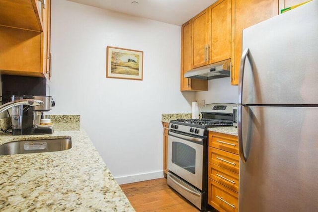 kitchen featuring stainless steel appliances, under cabinet range hood, a sink, light wood-type flooring, and baseboards
