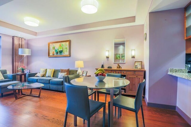dining area featuring wood finished floors, a raised ceiling, and baseboards