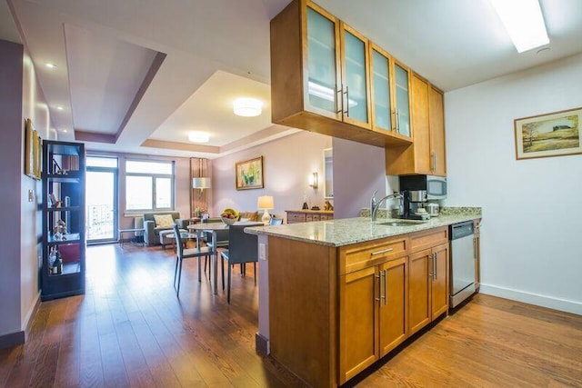 kitchen with appliances with stainless steel finishes, brown cabinetry, a sink, light stone countertops, and baseboards