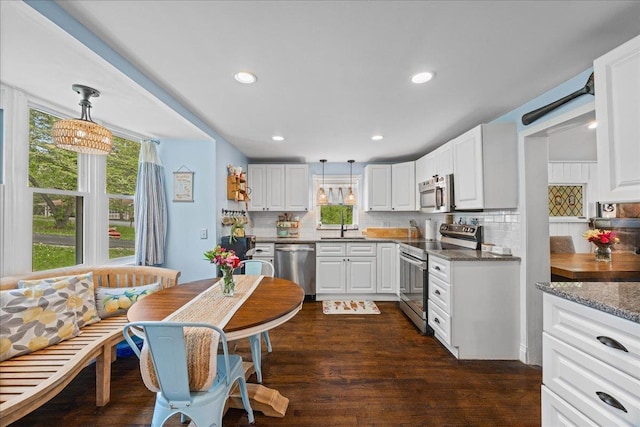 kitchen with stainless steel appliances, tasteful backsplash, white cabinetry, a sink, and hanging light fixtures