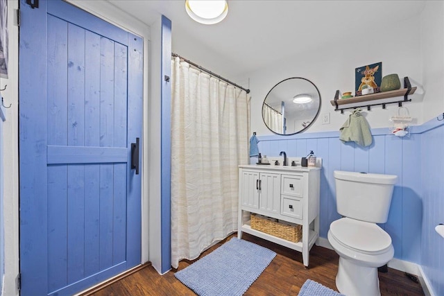 bathroom with wood finished floors, toilet, a wainscoted wall, vanity, and curtained shower