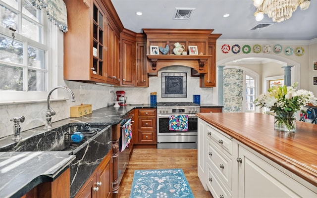 kitchen featuring stainless steel appliances, glass insert cabinets, arched walkways, decorative columns, and brown cabinets