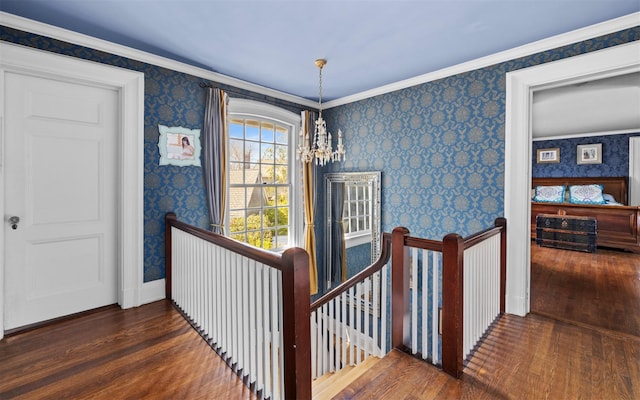 corridor featuring an upstairs landing, wallpapered walls, hardwood / wood-style flooring, a chandelier, and crown molding