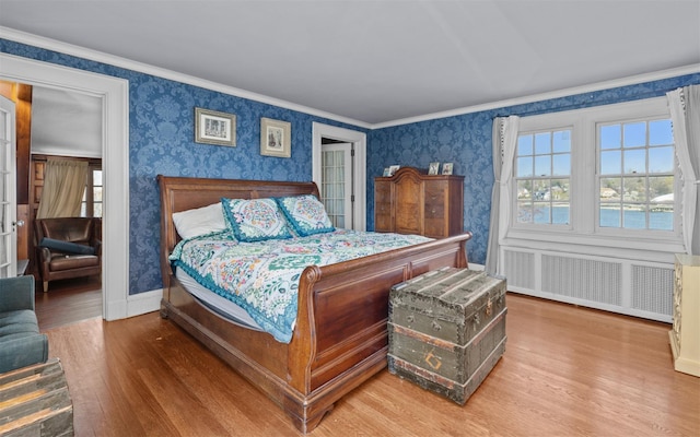 bedroom featuring wallpapered walls, wood finished floors, radiator, ornamental molding, and baseboards
