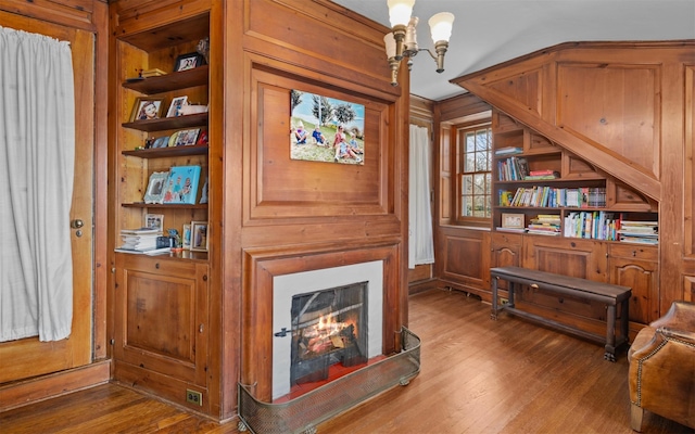 sitting room featuring wood finished floors, built in features, wooden walls, a lit fireplace, and a chandelier