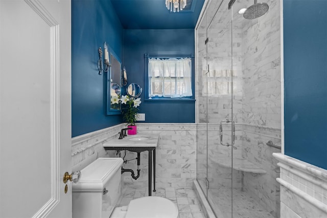 full bath featuring toilet, a sink, a shower stall, wainscoting, and marble look tiles