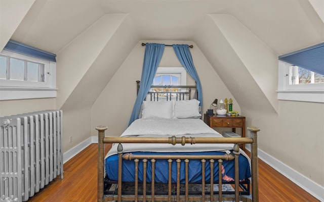 bedroom with radiator heating unit, wood finished floors, multiple windows, lofted ceiling, and baseboards