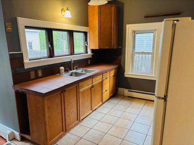 1358 Rte 44, Pleasant Valley, NY 12569 - kitchen with a baseboard heating unit, freestanding refrigerator, a sink, tile counters, and brown cabinetry