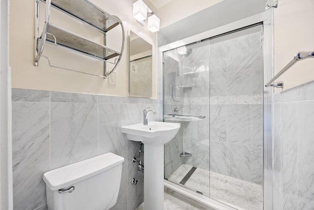 full bath with a stall shower, toilet, tile walls, and wainscoting