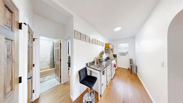 kitchen with white gas range oven, arched walkways, light wood-style floors, and baseboards