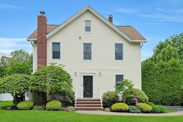 view of front facade with a chimney, entry steps, a shingled roof, and a front lawn