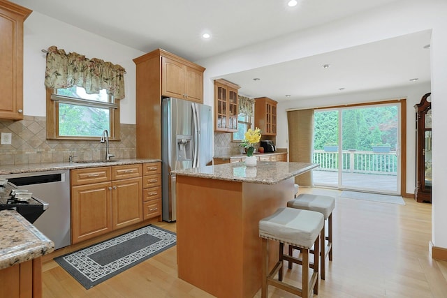kitchen featuring a sink, appliances with stainless steel finishes, light stone counters, a breakfast bar area, and light wood finished floors