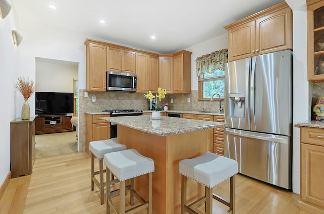 kitchen featuring stainless steel appliances, a sink, a center island, light wood-style floors, and a breakfast bar