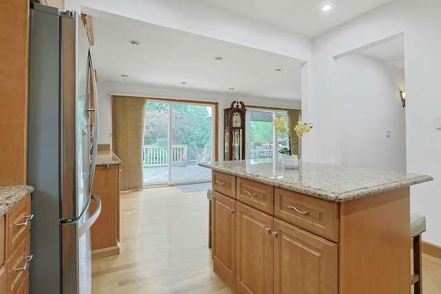 kitchen with freestanding refrigerator, light wood-type flooring, light stone countertops, a center island, and recessed lighting