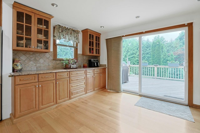 kitchen featuring tasteful backsplash, light wood-type flooring, light stone counters, glass insert cabinets, and brown cabinetry