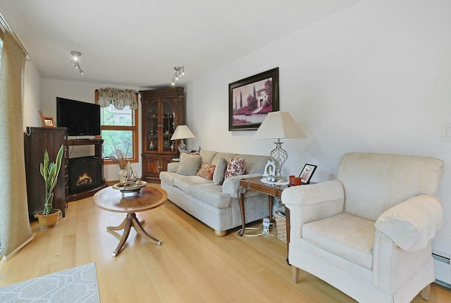 living room featuring wood finished floors, a baseboard heating unit, and a warm lit fireplace