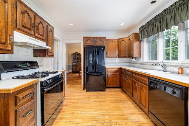 265 Brower Ave, Rockville Centre, NY 11570 - kitchen with black appliances, under cabinet range hood, light countertops, ornamental molding, and light wood-style floors