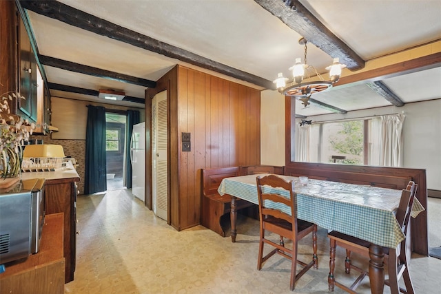 dining space with beam ceiling, a chandelier, and wood walls