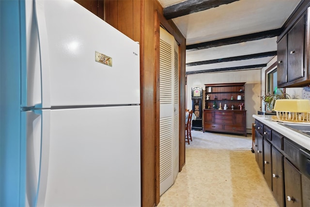 kitchen featuring freestanding refrigerator, beam ceiling, light countertops, and dark brown cabinetry