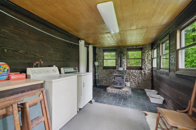 laundry area with wooden ceiling, independent washer and dryer, a wood stove, and wooden walls