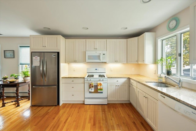 kitchen with white appliances, plenty of natural light, a sink, light stone counters, and recessed lighting