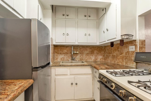 kitchen featuring gas range oven, freestanding refrigerator, a sink, tasteful backsplash, and light countertops
