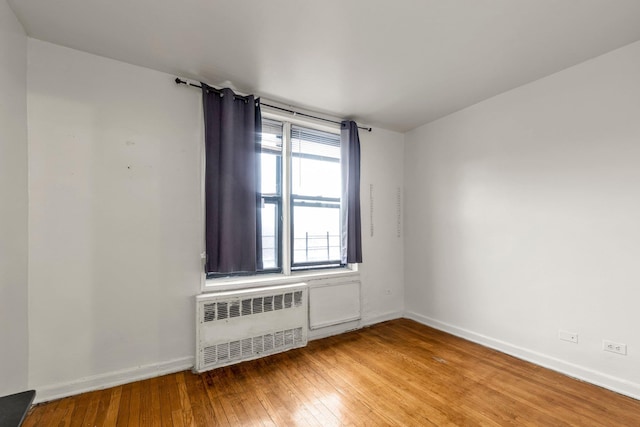 unfurnished room with radiator heating unit, light wood-style floors, and baseboards