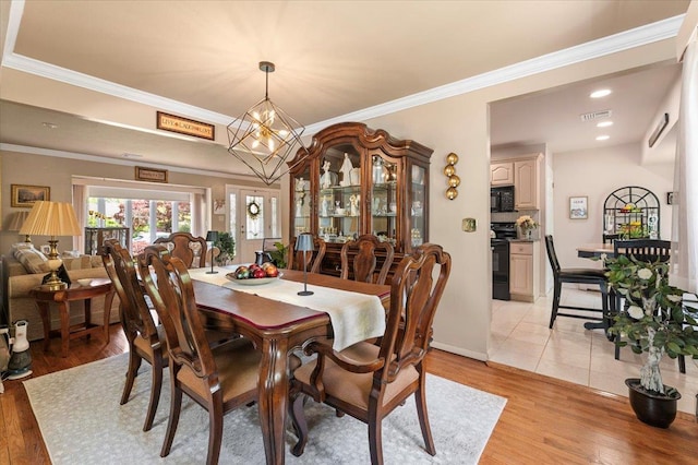 dining space featuring light wood-type flooring, a chandelier, crown molding, and baseboards