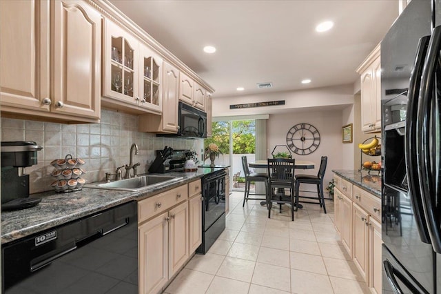 kitchen featuring black appliances, a sink, light tile patterned flooring, decorative backsplash, and glass insert cabinets