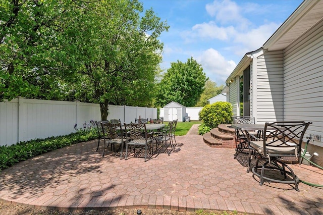 view of patio / terrace featuring outdoor dining area, a storage unit, a fenced backyard, and an outdoor structure