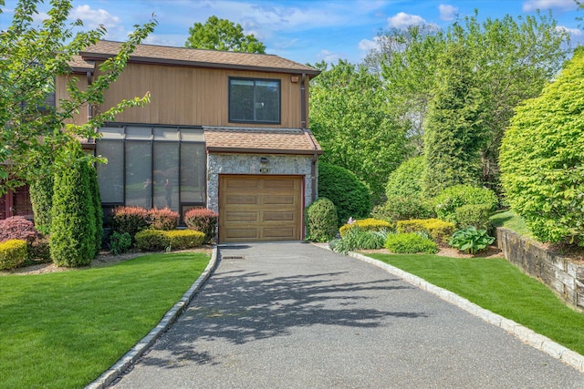 view of front of property featuring an attached garage, asphalt driveway, a front lawn, and roof with shingles