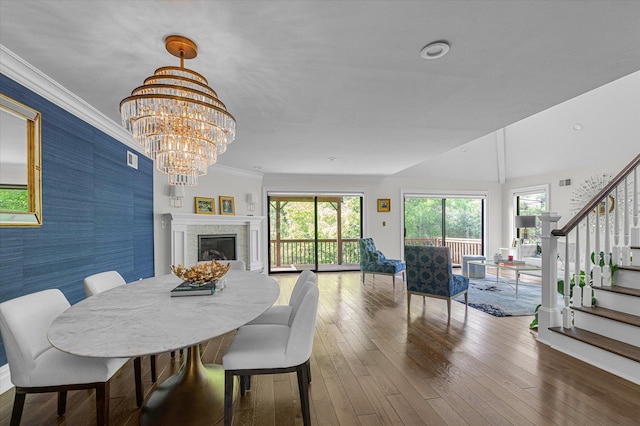 dining area featuring stairs, wood finished floors, a chandelier, a fireplace, and an accent wall