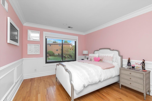 bedroom featuring light wood-style floors, a wainscoted wall, and crown molding