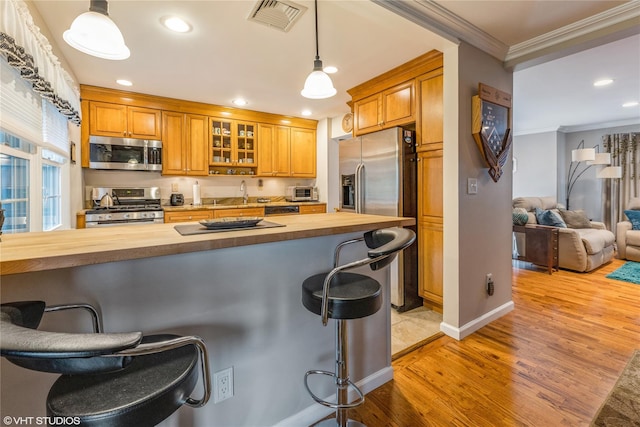 kitchen featuring appliances with stainless steel finishes, wooden counters, crown molding, a breakfast bar, and light wood finished floors