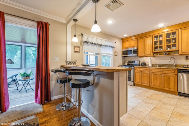 kitchen with appliances with stainless steel finishes, crown molding, brown cabinetry, plenty of natural light, and glass insert cabinets