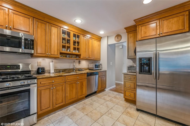 kitchen featuring appliances with stainless steel finishes, brown cabinets, stone counters, recessed lighting, and a sink