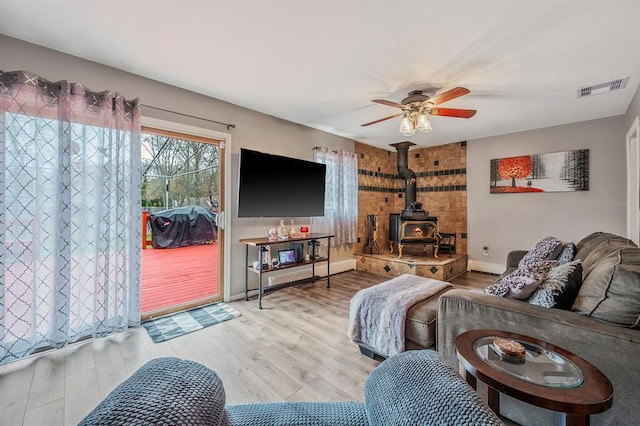 living area featuring a wood stove, ceiling fan, wood finished floors, and baseboards
