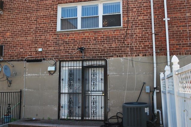 doorway to property featuring central AC unit, brick siding, and fence