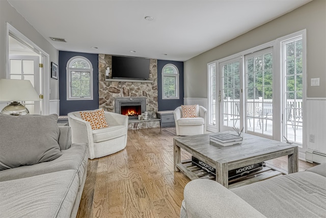 living room featuring light wood finished floors, a wainscoted wall, plenty of natural light, a baseboard heating unit, and a fireplace